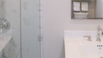 A bathroom with a glass shower enclosure, a white sink with a mirror above it, and a towel rack with folded towels.