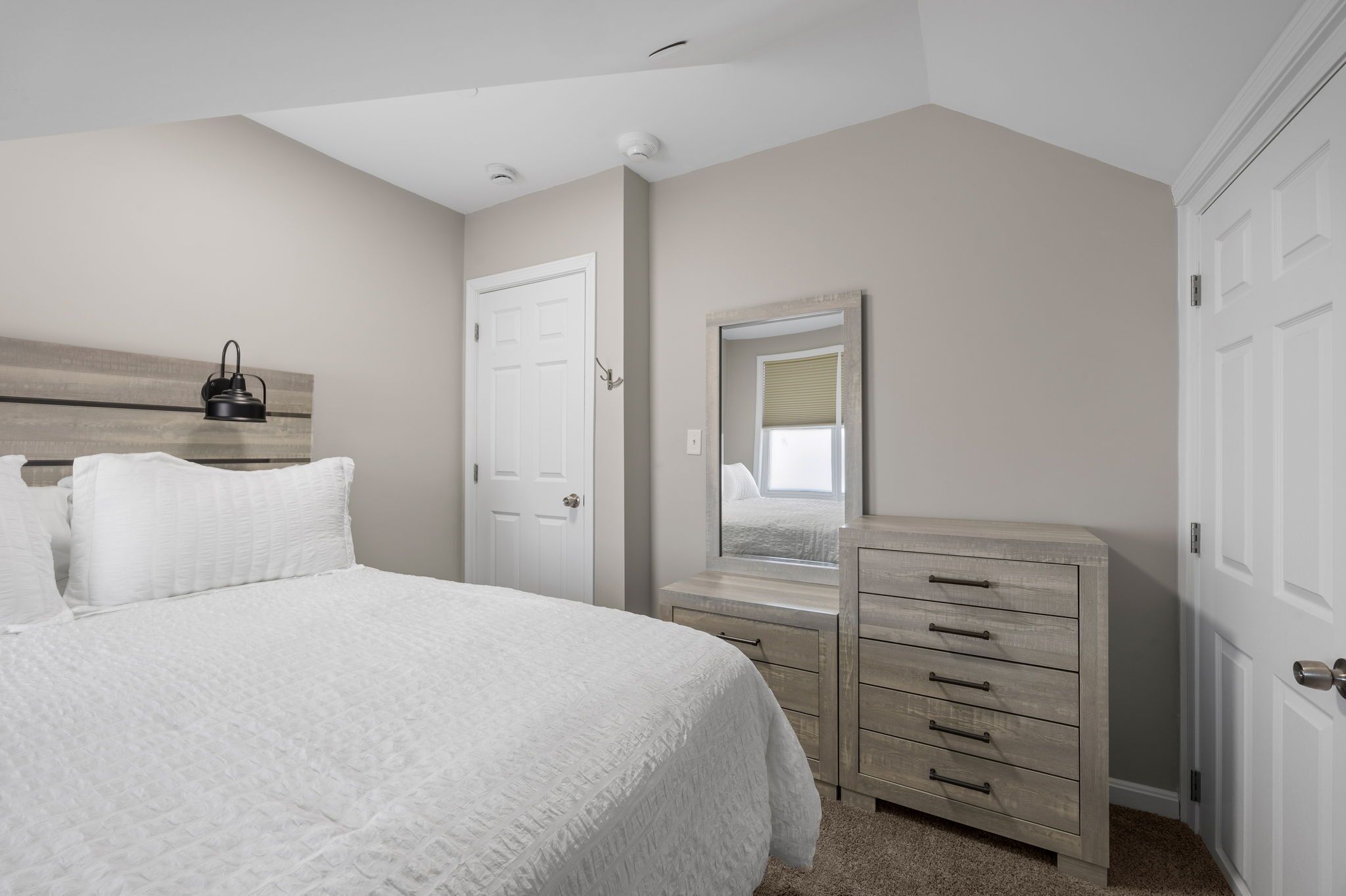 A bedroom with a bed, dresser, mirror, and a door.