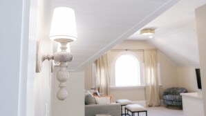 A room with a white wall-mounted lamp, a window with curtains, a sofa, and a patterned chair. - The Bell Inn (Peabody)