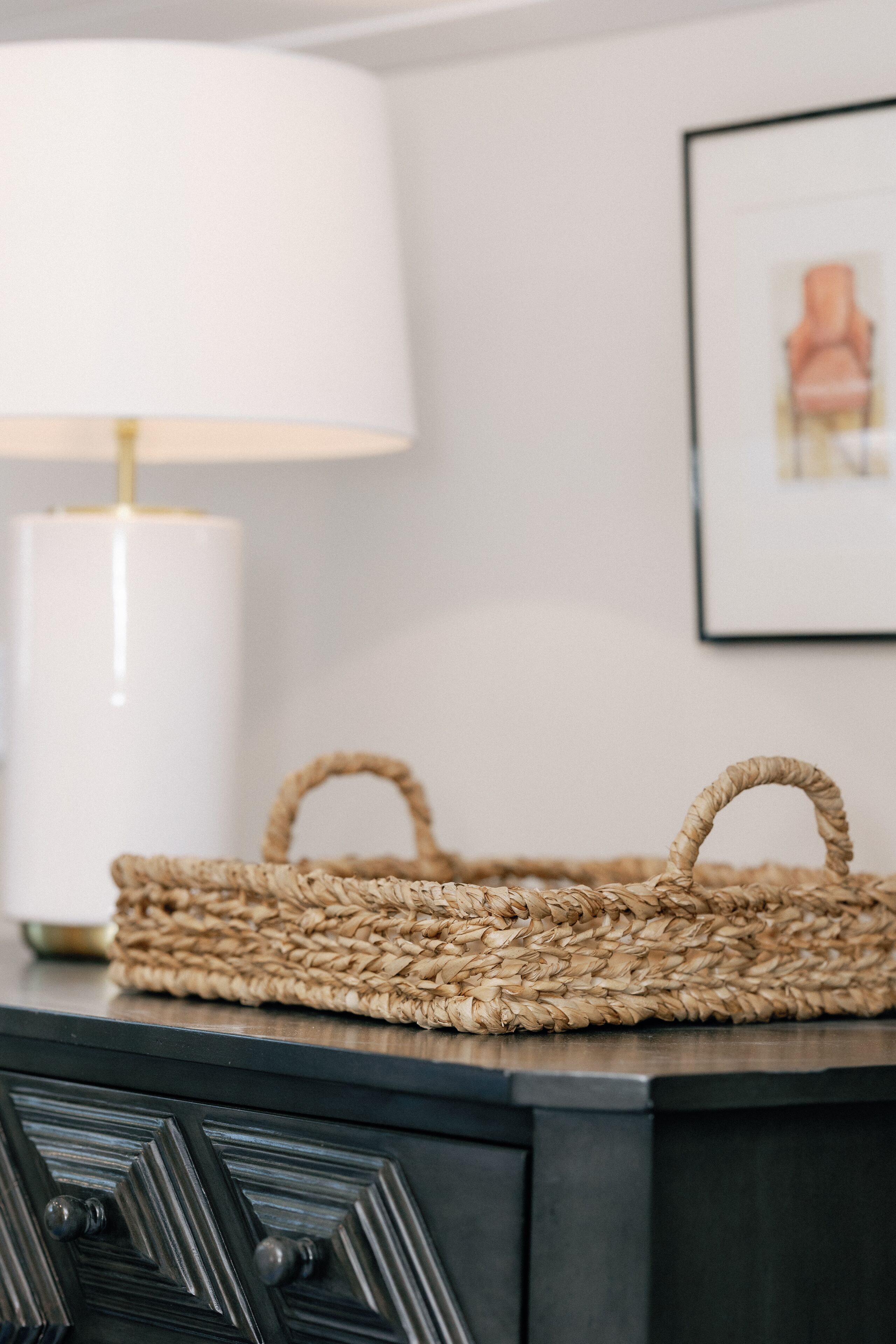 A woven basket on a dark wooden surface with a white lamp in the background.