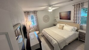 Ein Schlafzimmer mit einem Bett, Nachttischen, einem Schreibtisch, einem Stuhl, einem Deckenventilator und einem Fenster mit Vorhängen.