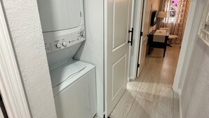 Ein Waschraum mit Waschmaschine und Trockner, einer Schiebetür und Blick in einen Essbereich mit Tisch und Stühlen.