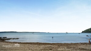 Una playa con aguas tranquilas, barcos y una costa lejana.