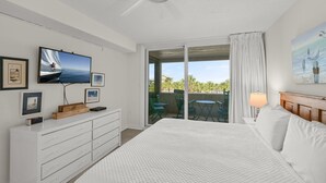 Ett hotellrum med en stor säng, en tv som är monterad på väggen, en byrå i trä och en balkong med utemöbler.