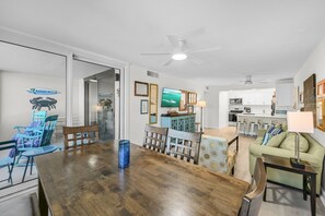 Un amplio salón con una mesa de comedor de madera, sillas, un sofá y una cocina al fondo.