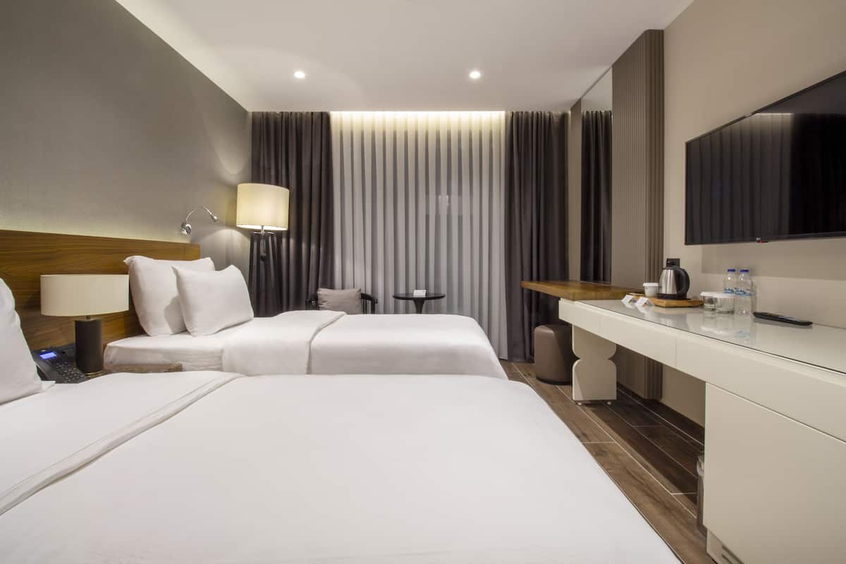 Quarto de hotel com duas camas, uma mesa, uma cadeira, um abajur, uma televisão e um espelho.