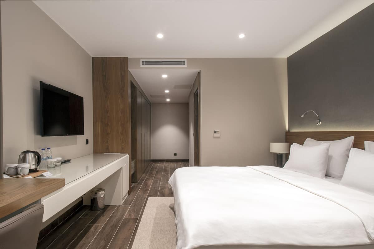 Quarto de hotel com cama, televisão, escrivaninha com cafeteira e lixeira.