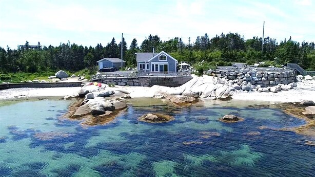 Une étendue d’eau claire parsemée de rochers, une maison et, au fond, une zone boisée.