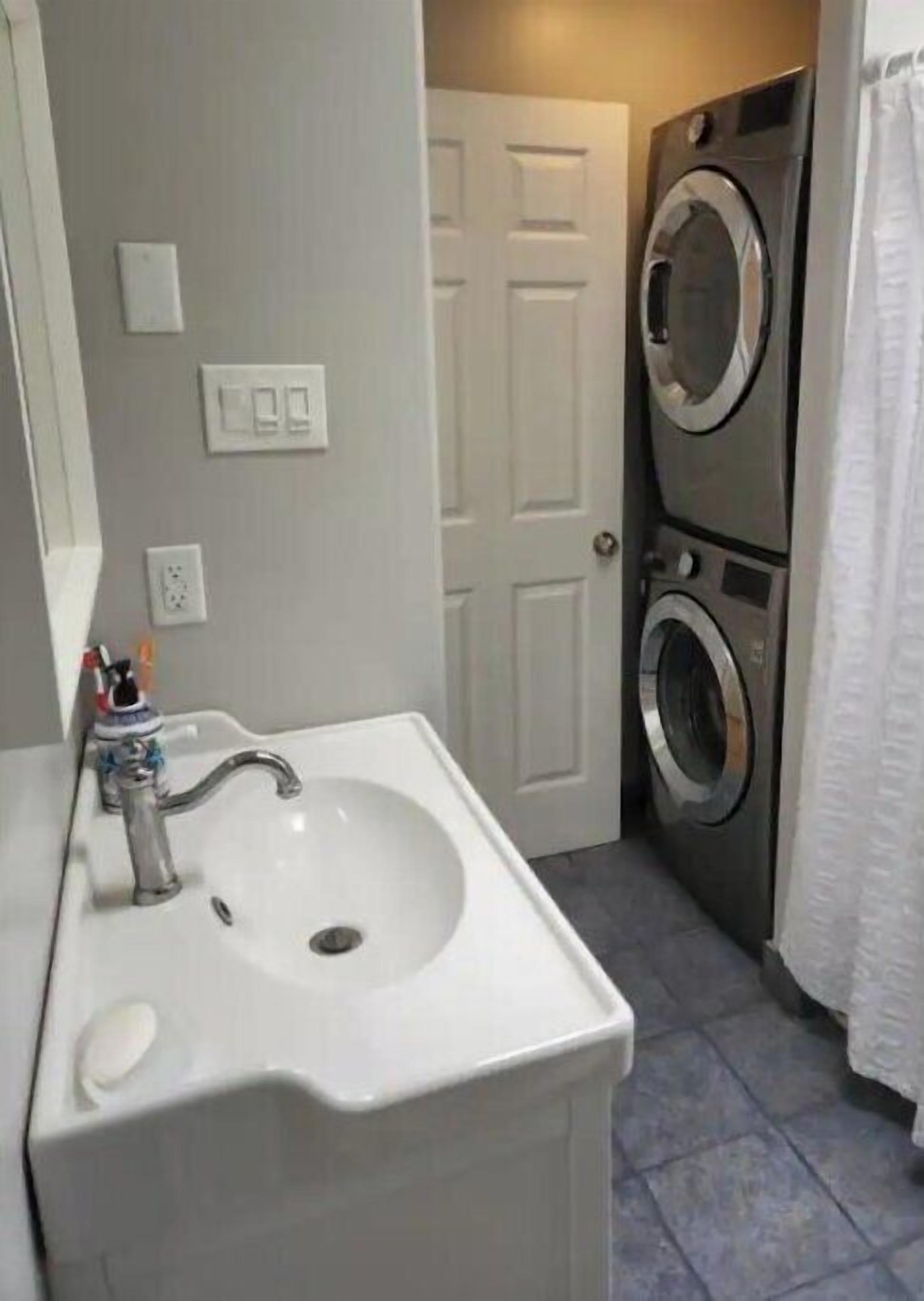 A bathroom with a sink, two stacked washing machines, and a door.