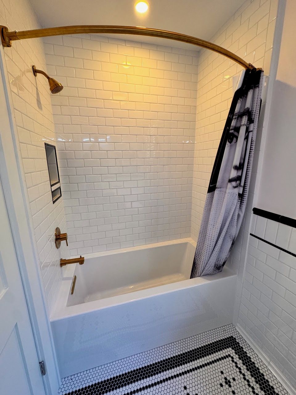A modern bathroom with white subway tile walls, a white bathtub, and a black and white patterned floor.
