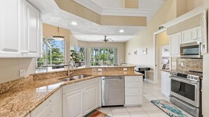 A modern kitchen with white cabinets, granite countertops, stainless steel appliances, and a view to the outdoors. - Mile From Beach Access, Spacious and Redone, Heated Pool! (Marco Island)
