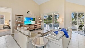 A spacious living room with a large flat-screen TV, a wooden entertainment unit, and a comfortable seating area with a coffee table. - Mile From Beach Access, Spacious and Redone, Heated Pool! (Marco Island)