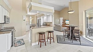 A spacious kitchen with a central island, bar stools, and a dining area with a glass door leading outside. - Mile From Beach Access, Spacious and Redone, Heated Pool! (Marco Island)