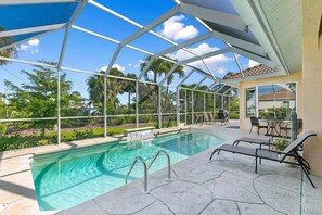 Piscina con cerramiento de vidrio, sillas de descanso y zona de patio con mesa y sillas.