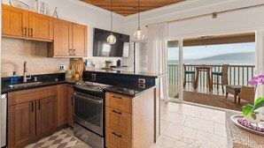 Una cocina con armarios de madera, encimera negra, electrodomésticos de acero inoxidable y vistas a un balcón con mobiliario exterior.