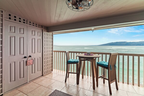 A balcony with a view of the sea, a wooden table, two chairs, and a door with a sign.