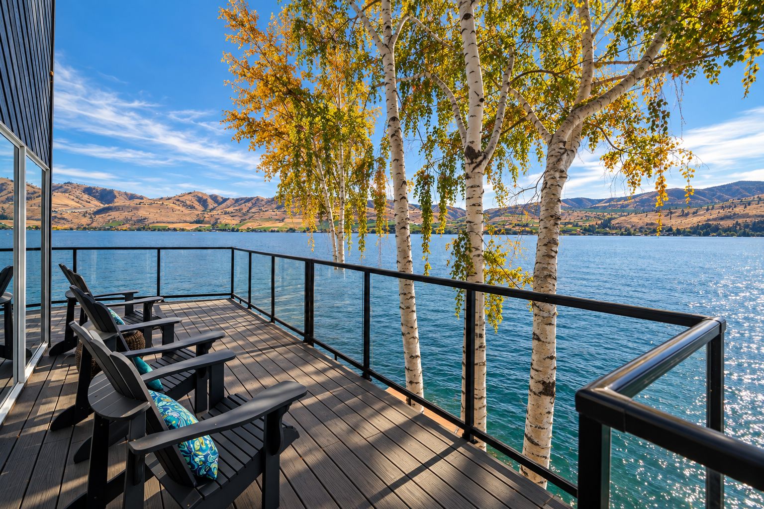 Una terraza con mobiliario exterior y vistas a un lago, árboles y colinas al fondo.
