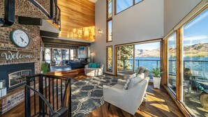 A spacious living area with a fireplace, a large window overlooking a lake, and a cozy seating arrangement. - Premier home, Waterfront, Views, Hot Tub, Dogs OK (Lake Chelan)
