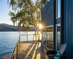 A wooden deck with a glass door leading to a room, overlooking a lake with mountains in the background. - Premier home, Waterfront, Views, Hot Tub, Dogs OK (Lake Chelan)