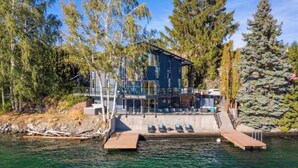 A modern house with a deck extending over water, surrounded by trees. - Premier home, Waterfront, Views, Hot Tub, Dogs OK (Lake Chelan)