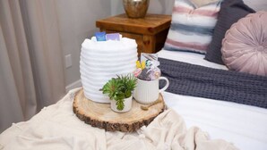 Ein gemütliches Schlafzimmer mit Bett, Nachttisch mit Lampe und einer dekorativen Anordnung auf einer Holzbrett.