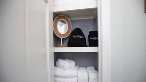 Ein Schrank mit Regalen, der einen Haartrockner, eine Kosmetiktasche und gefaltete Handtücher beherbergt.