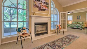 A spacious living room with a fireplace, large windows, and a bed with a tropical bedspread. - 16th and Golden in Diamondhead (Diamondhead)
