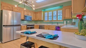 A modern kitchen with wooden cabinets, a stainless steel refrigerator, a central island with a bowl of fruit, and a microwave above the stove. - 16th and Golden in Diamondhead (Diamondhead)