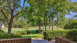 A brick pathway leading to a golf course with lush greenery and trees. - 16th and Golden in Diamondhead (Diamondhead)