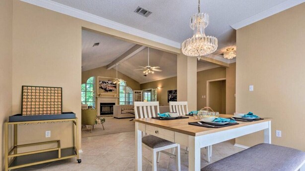 A spacious dining area with a wooden table set for four, white chairs, and a chandelier. - 16th and Golden in Diamondhead (Diamondhead)