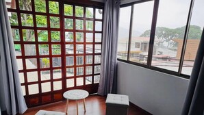 A room with a large window, a small round table, two ottomans, and a view of greenery and buildings outside. - CASA DEL ARBOL ESCAZU (San Antonio)