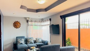 A modern living room with a sofa set, a flat-screen TV, and a large window with a view of the outside. - CASA DEL ARBOL ESCAZU (San Antonio)