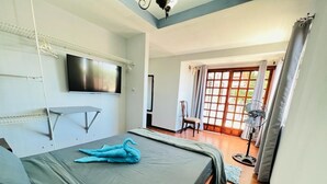 A bedroom with a bed, a TV mounted on the wall, a fan, and a view of the outside through a window. - CASA DEL ARBOL ESCAZU (San Antonio)