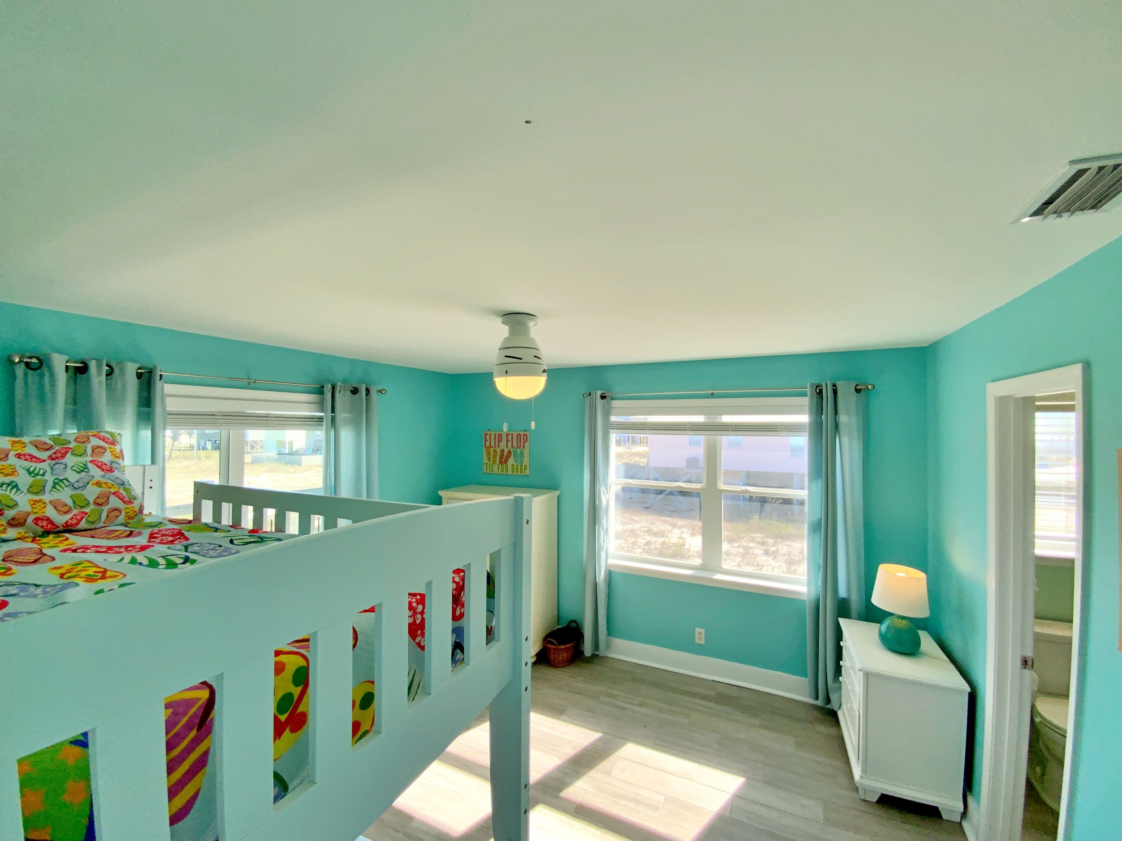 A child's room with a bunk bed, a window with curtains, a small bedside table with a lamp, and a view of the outdoors.
