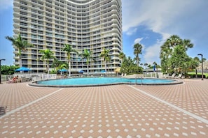 Ein großes Hotel mit gewölbter Fassade, einem Schwimmbad und Palmen.