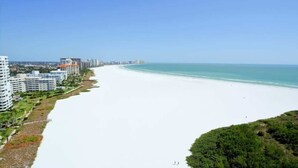 Un paysage urbain côtier avec une vaste plage, de hauts immeubles et un ciel dégagé.