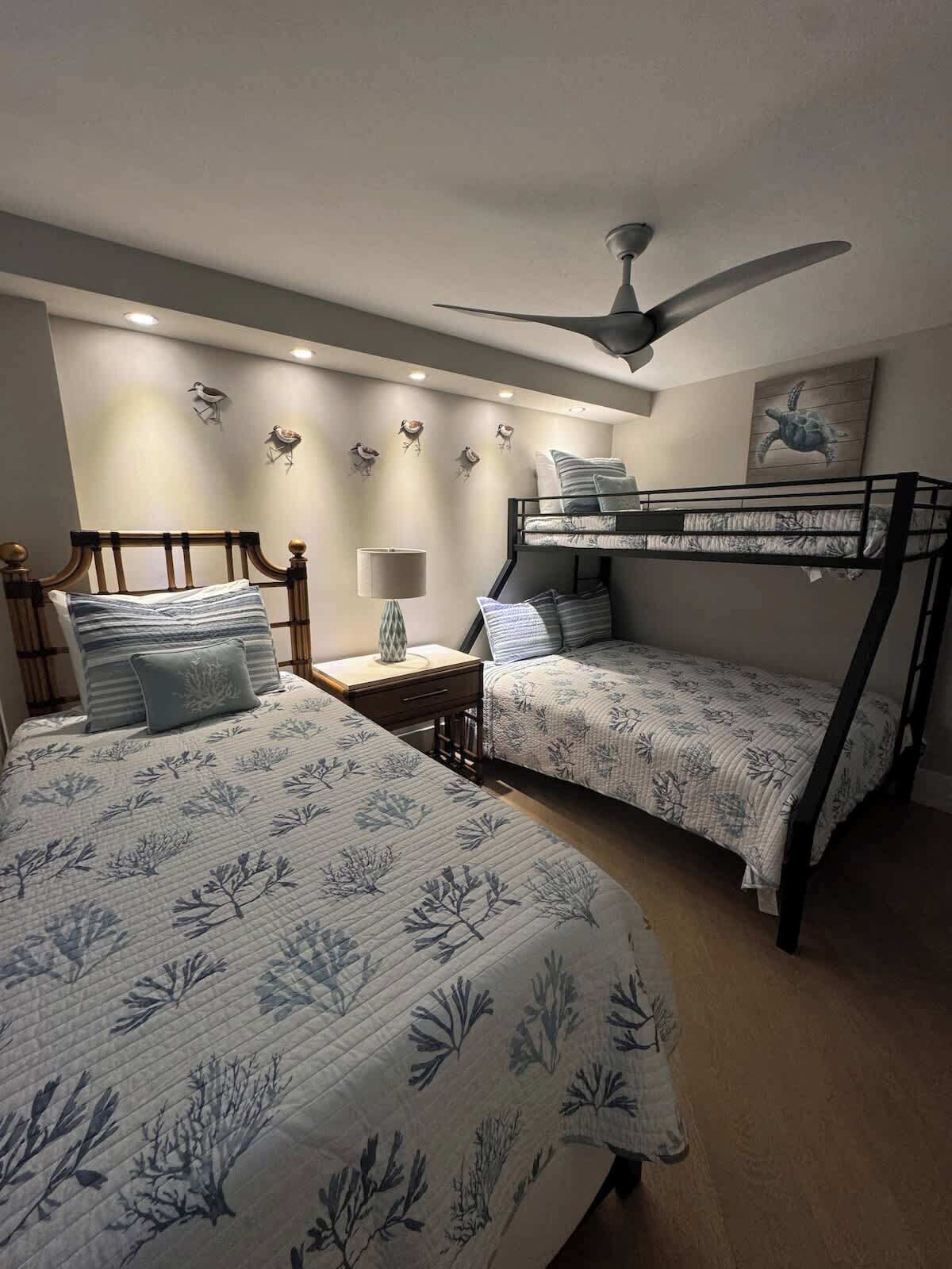Une chambre avec deux lits, un ventilateur de plafond, des décorations murales représentant des oiseaux et un tableau représentant une tortue.