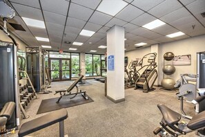 Ein Fitnessstudio mit unterschiedlicher Trainingsausstattung, großen Fenstern und Blick auf Grünfläche.