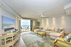 A modern living room with a large flat-screen TV, a beige sectional sofa, a small coffee table, and a decorative rug. - Beautiful SST3 beachfront condo. (Marco Island)