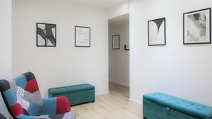 Ein modernes Zimmer mit einem petrolfarbenen Sofa, passendem Hocker und abstrakter Kunst an den Wänden.