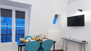 Un coin repas avec une table dressée pour deux personnes, un téléviseur fixé au mur et une fenêtre dotée de vitres teintées en bleu.