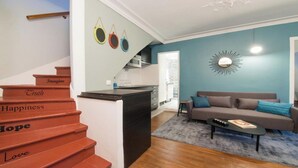 Un salon moderne avec un escalier, un canapé, une table basse et un coin cuisine à l’arrière-plan.