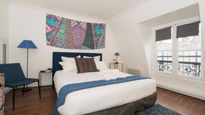 Une chambre à coucher bien rangée, avec un grand lit, une chaise, une table de chevet et une fenêtre donnant sur un beau paysage.