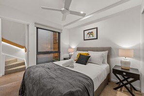 Cozy retreat with a large bed, ceiling fan, and nightstand with a lamp, plus a window and staircase.