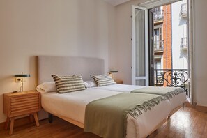 A bedroom with a bed, bedside tables, a nightstand, a balcony with a railing, and a view of a building. - Always Easy I San Marcial (San Sebastián/Donostia)
