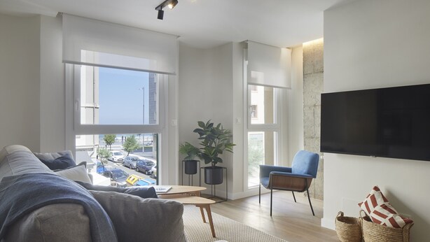 Un salon moderne avec un canapé, une table basse, un téléviseur fixé au mur et une vue sur la rue.