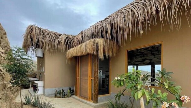 A building with a thatched roof, a stone pathway, and a small garden with plants and flowers. - Villa-neem. Amplia, Cómoda y Tranquila (Piura)