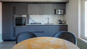 Una cocina moderna con armarios grises, horno empotrado, microondas y salpicadero de mármol. En primer plano, hay una mesa redonda con dos sillas.