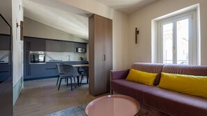Una sala de estar moderna con un sofá y una mesa de centro, una zona de cocina con armarios y electrodomésticos, y un comedor con sillas.