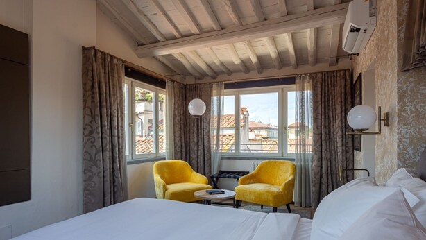 Una habitación de hotel con una cama, dos sillones amarillos, una mesita y una ventana con cortinas.